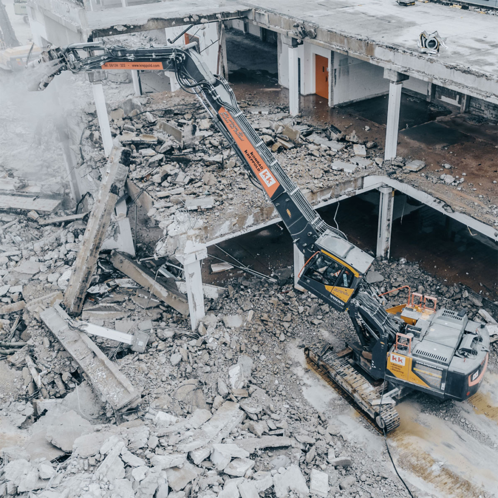 Bagger mit Abbruchausrüstung, ausgefahrenem Teleskopfahrwerk und hochgefahrener und gekippter Kabine