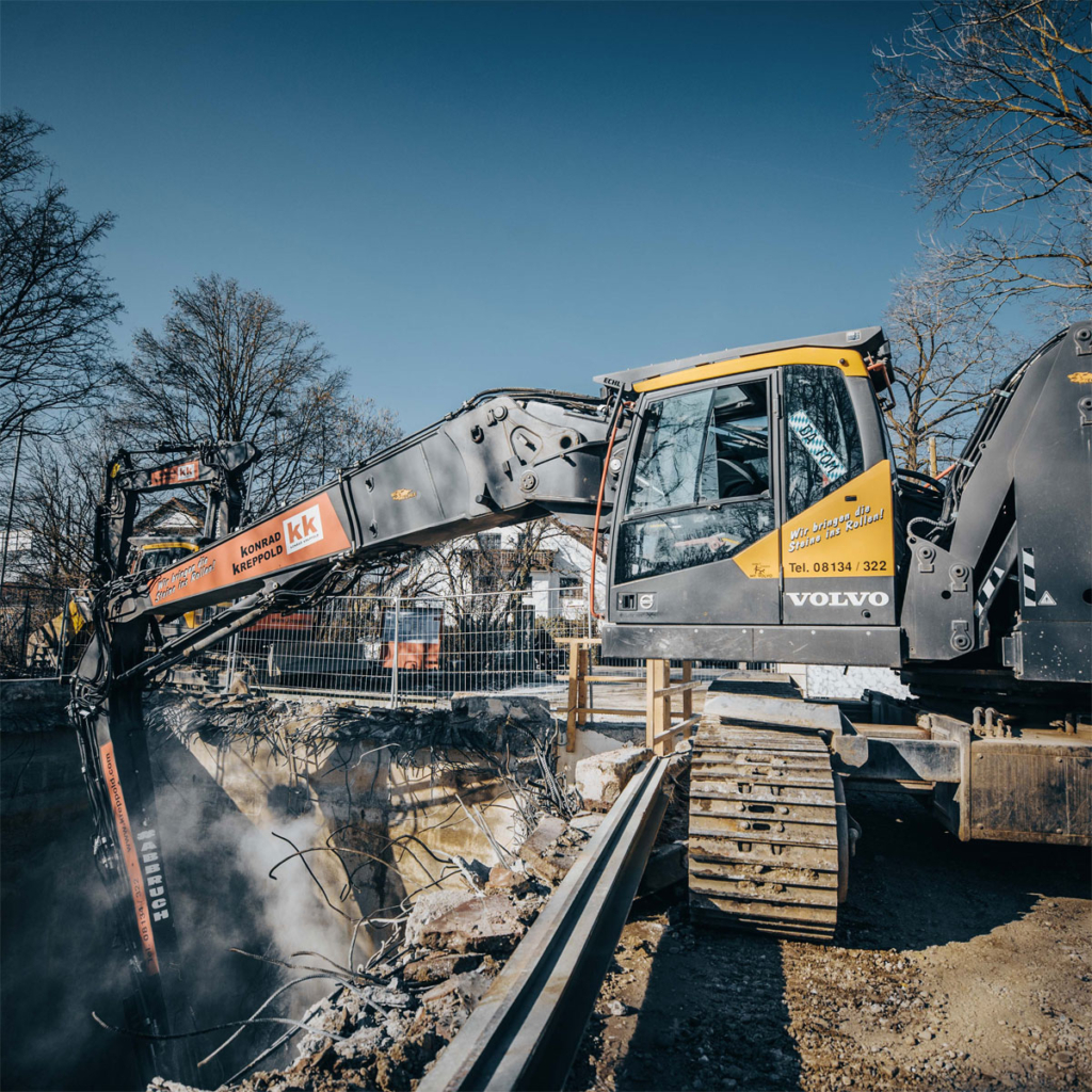 Bagger mit Abbruchausrüstung und ausgefahrenem Teleskopfahrwerk beim Tiefbau