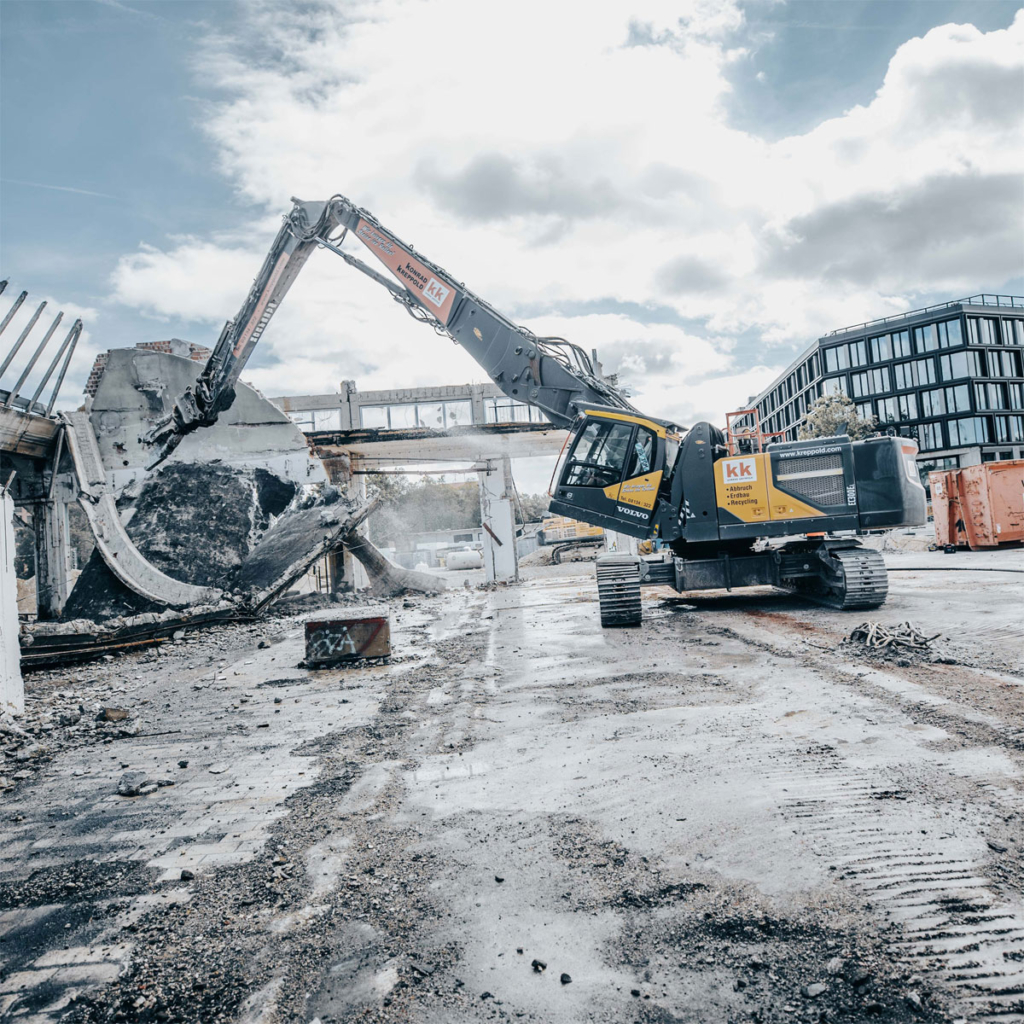 Bagger mit Abbruchausrüstung, ausgefahrenem Teleskopfahrwerk und gekippter Kabine